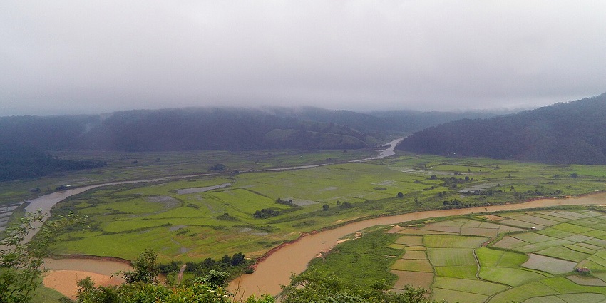 Lalong eco-park from above with brown curvy river, green grass plains and mountains.