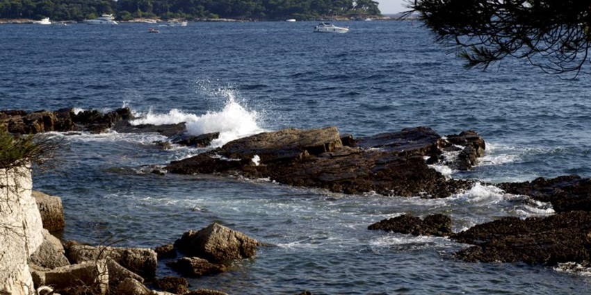 View of Île Saint-Honorat from Île Sainte-Marguerite with calm sea and clear blue sky.