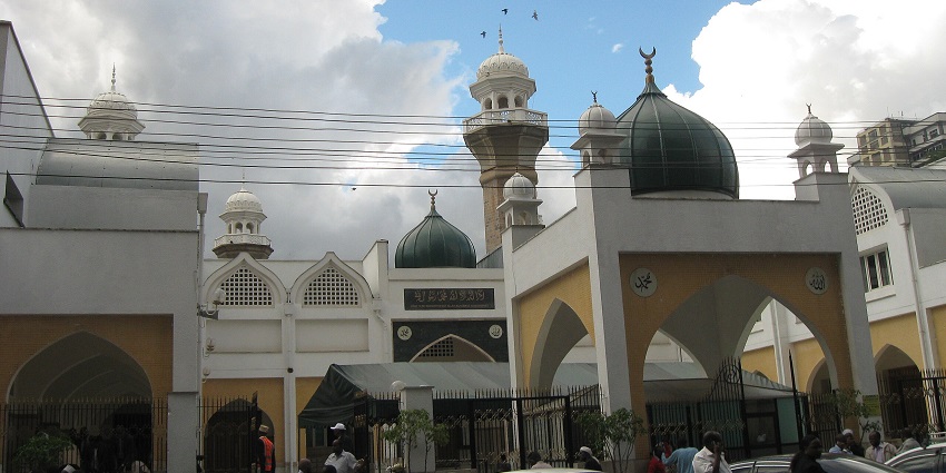 Jamia Mosque in Nairobi, with numerous parked cars under a vibrant blue, cloudy sky.
