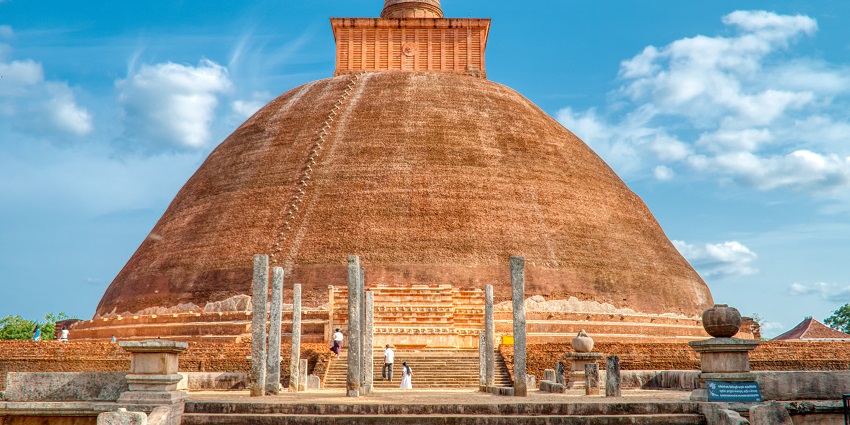 The Jetavanaramaya Stupa in Sri Lanka, a large ancient brick structure with a rounded dome against a clear blue sky.