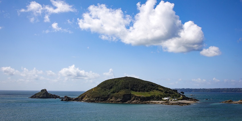 A lush green island rising from the blue sea under a bright sky with scattered clouds.