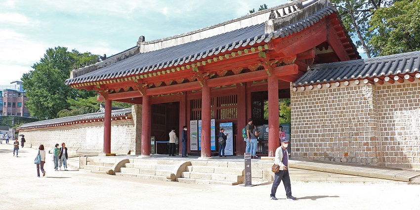 Entrance to the Jongmyo shrine with signages, people standing and walking on the entrance