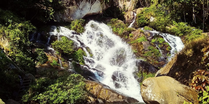 Waterfalls in Assam with water flowing on the rocky surface and green grass growing on the rocks