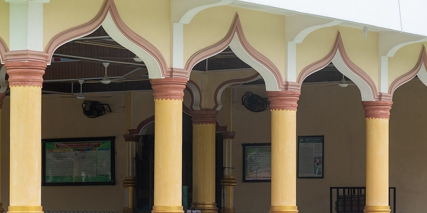 Yellow pillars of a mosque with its inside hall visible from the outside and pictures hanging