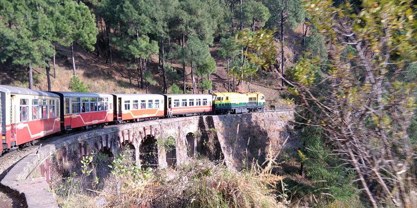 Alt text: A scenic train on the Kalka–Shimla Railway, showcasing stunning views and historic Himalayan travel charm.
