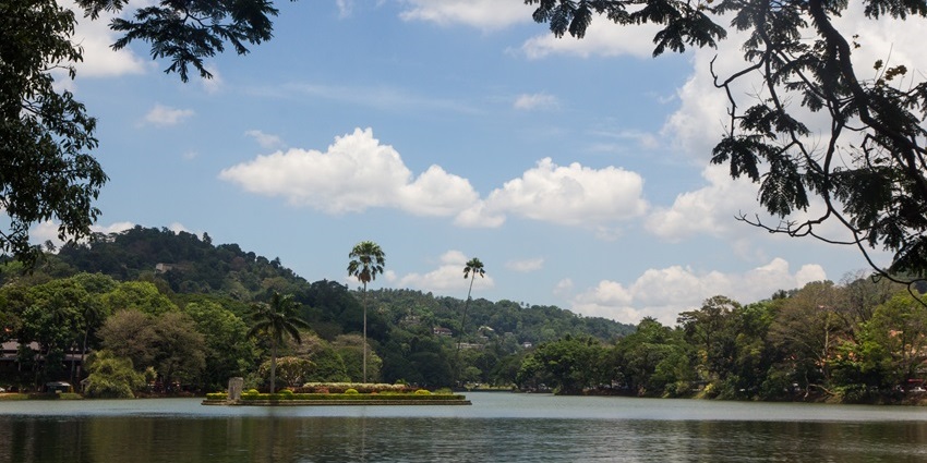 Calm waters of Kandy Lake with trees and lush green mountains in the background