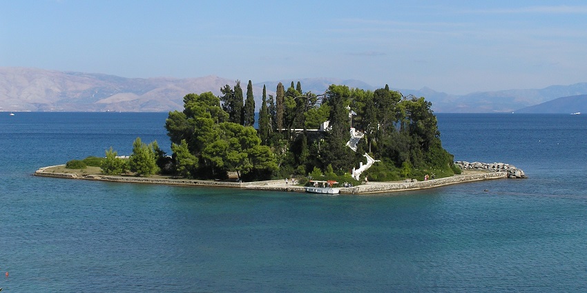 Small tree-covered island with stone dock, surrounded by a calm blue sea.