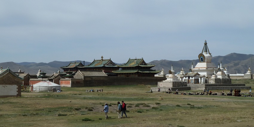 Multiple people walking at the ruins of Karakorum with buildings in the back and green plains