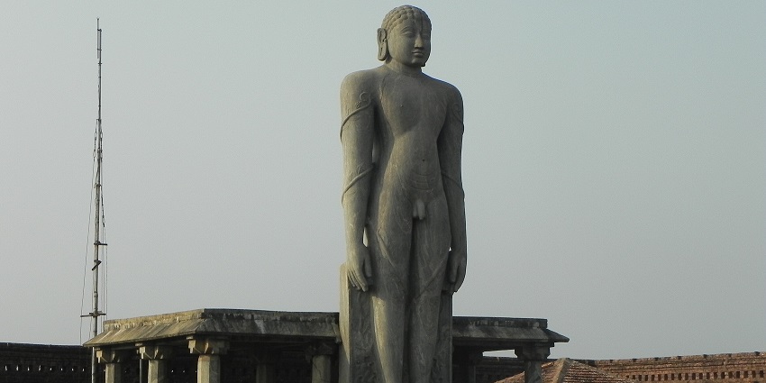 The giant stone Gomateswara statue is at the top of the platform under the clear sky.