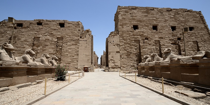 Entrance of Karnak Temple in Luxor, Egypt, with ram-headed sphinx statues under the clear sky.