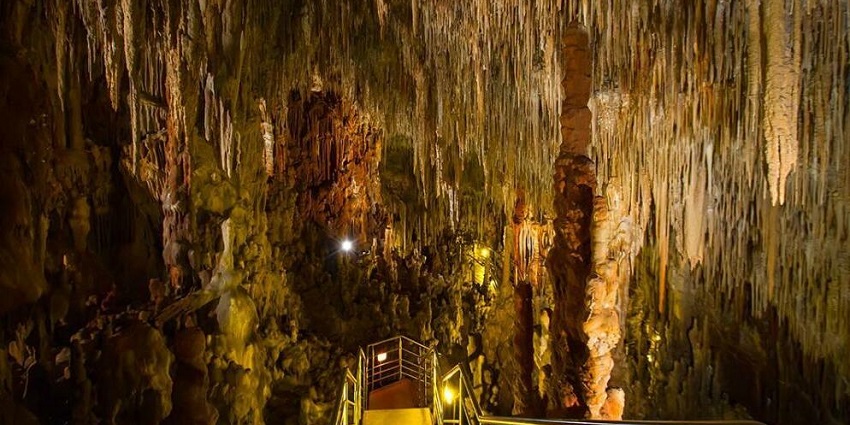 Inside of Diros cave in Greece with sharp stalactites, reflective water and lights.