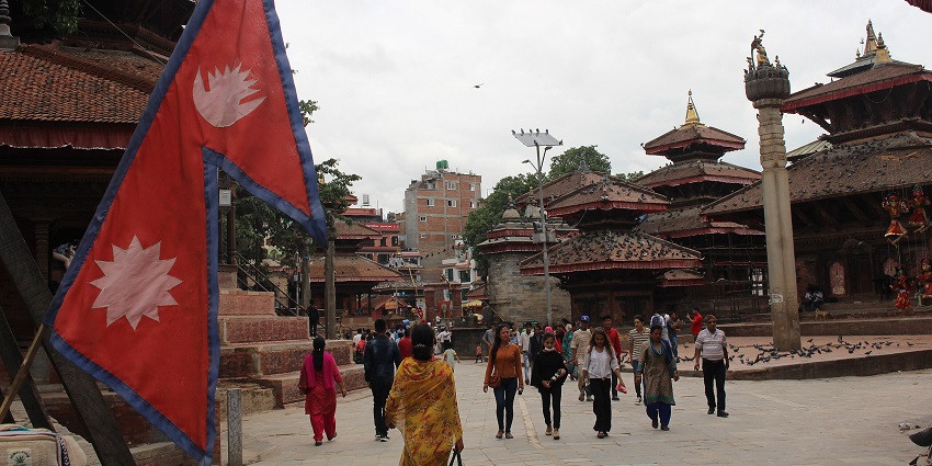 Kathmandu Durbar Square with many visitors, a flag on the left, and birds sitting all over.