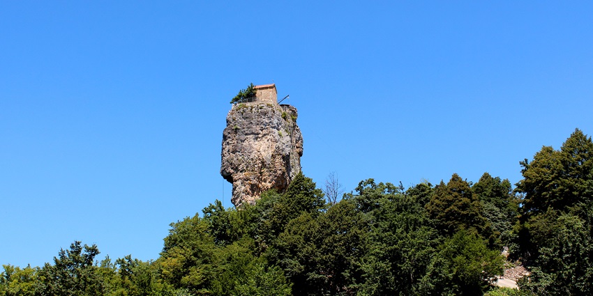 A narrow limestone column topped with a tiny church perched over the forested hillside.