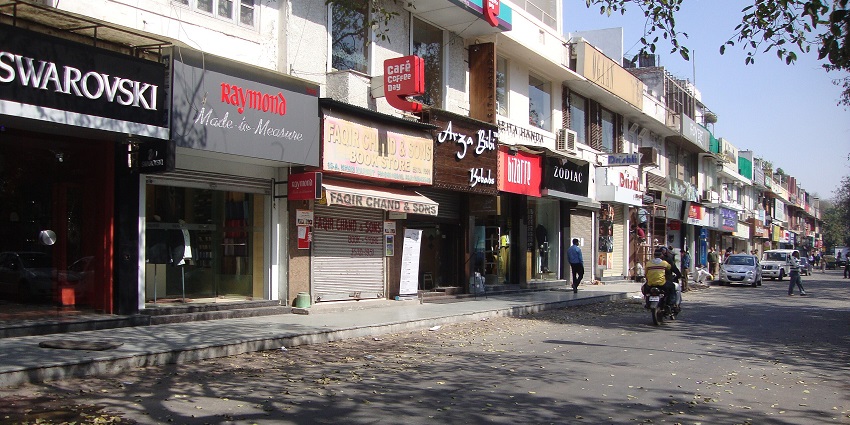 Streets in Khan Market with multiple signboards, shops, and people standing.