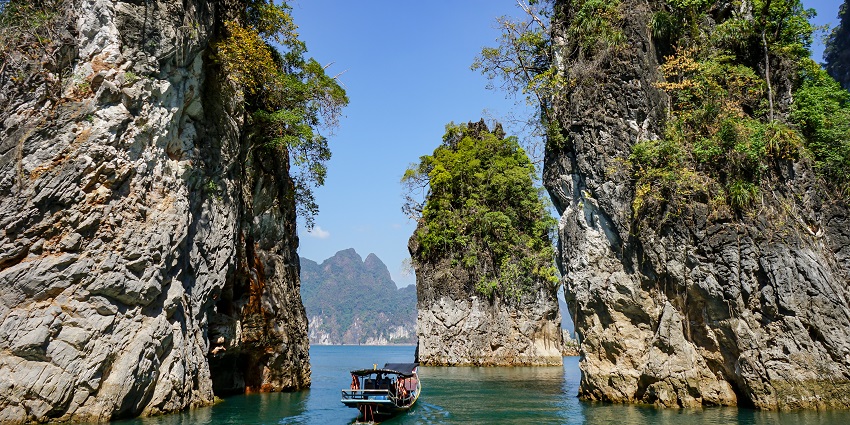 Khao Sok National Park with people in a boat, tall rocky cliffs, and greenery on the rocks.