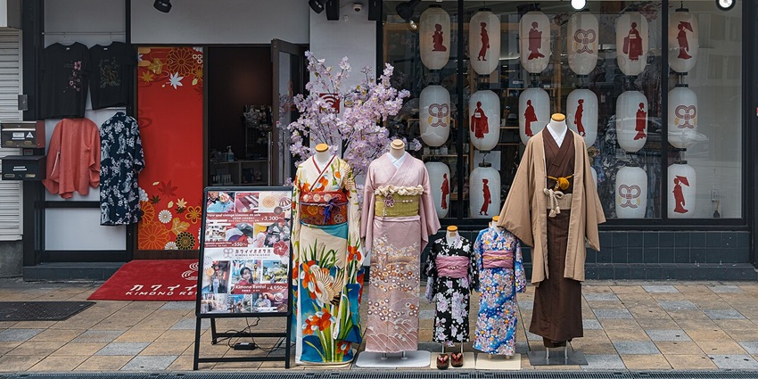 Woman wearing a blue yukata with floral prints, standing outside a Japanese-style building.