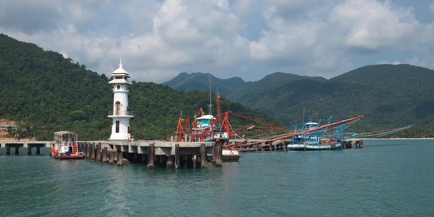 Bang Bao Pier in Ko Chang with a white architectural building of the lighthouse and green hills.