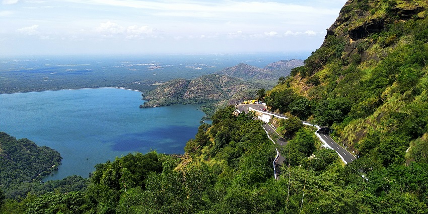 Misty aerial view of Kodaikanal Lake surrounded by lush greenery and forested hill slopes.

