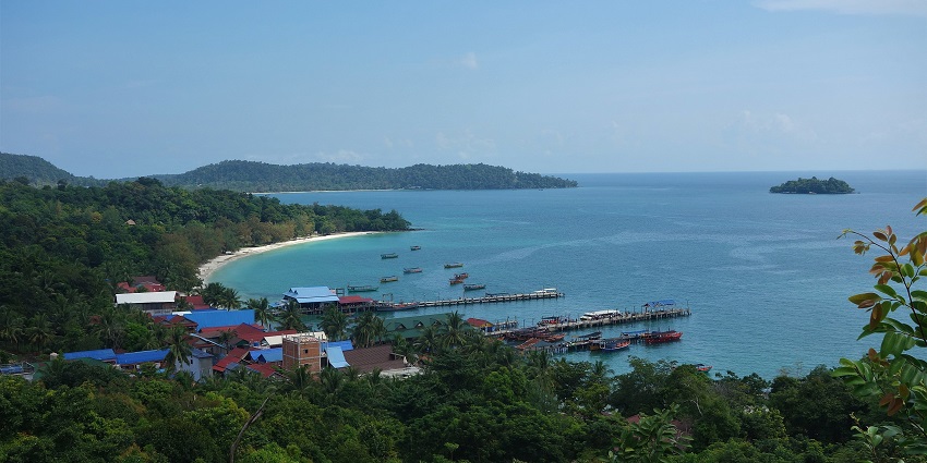 Scenic view of a lush coastal village with docks and boats along the turquoise waters of the islands in Cambodia.