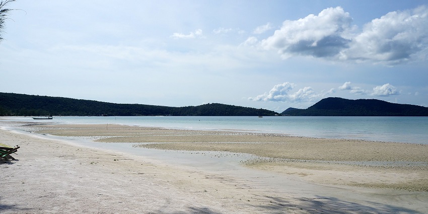 A serene sandy beach with shallow waters and distant hills on one of the tranquil islands in Cambodia.
