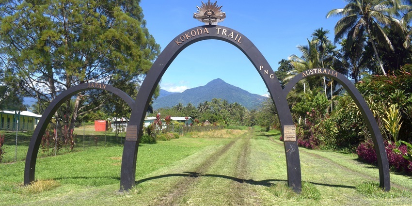 The entrance of the Kokoda Trail with distant buildings, palm trees and mountains, one of the historical places in Papua New Guinea.