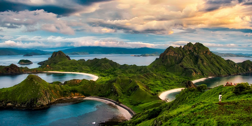 Rocky coastline with clear blue waters, green hills, and one of the places to visit in Indonesia in December.