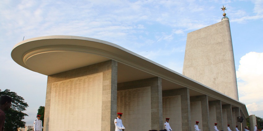 Kranji War Memorial with white grave markers, green lawns, and a tall memorial structure under a clear blue sky.