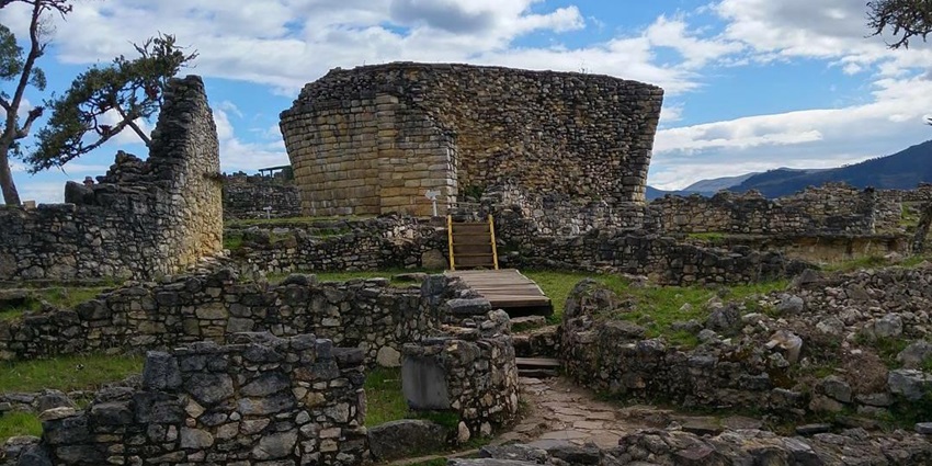 Ancient circular stone structures of the Kuelap stand atop a hill under a blue sky, Peru.