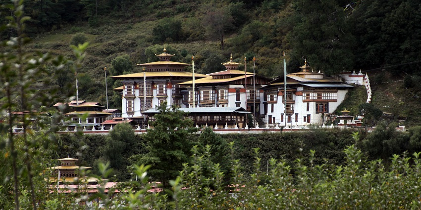 Multi-tiered monastery complex set among pine-covered hills with golden rooftops.