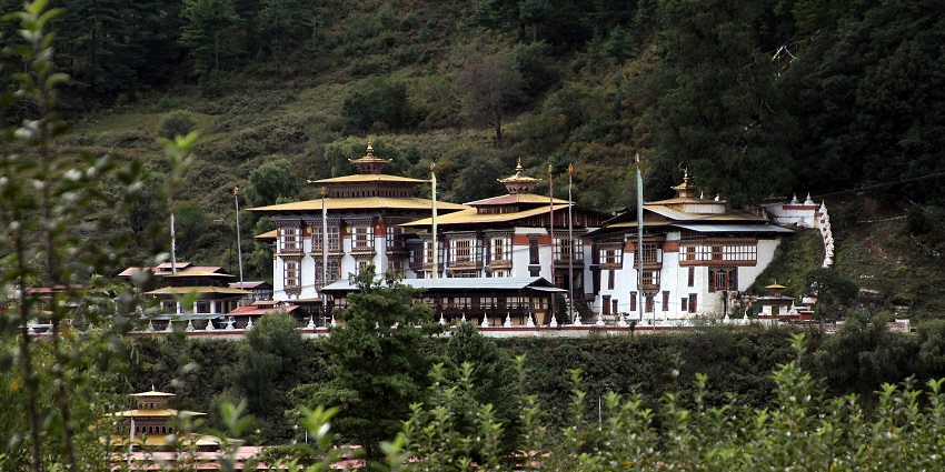 Kurjey Lhakhang in Bumthang with distant white architectural buildings and dense greenery.