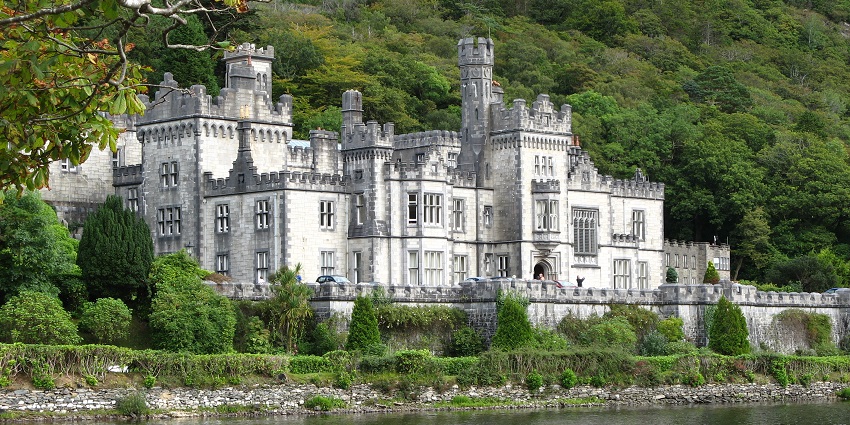 Beautiful white and grey Kylemore Abbey with a serene river in front in lush greenery