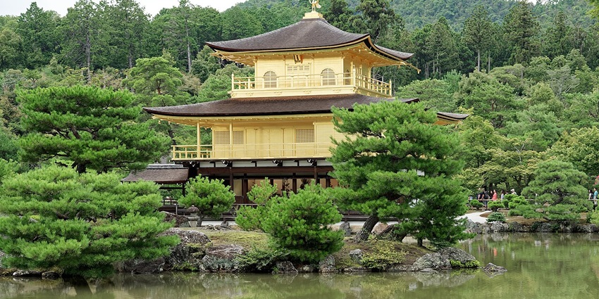 The Golden Temple by a tranquil pond, surrounded by lush green trees and forested hills, is one of the best historical places in Japan.