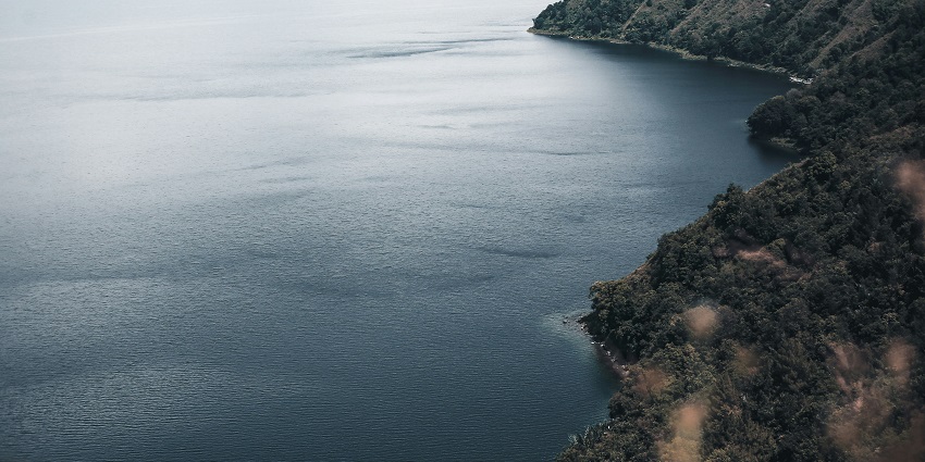 A clear blue lake, surrounded by green hills and dramatic skies, a breathtaking natural place to visit in Indonesia.
