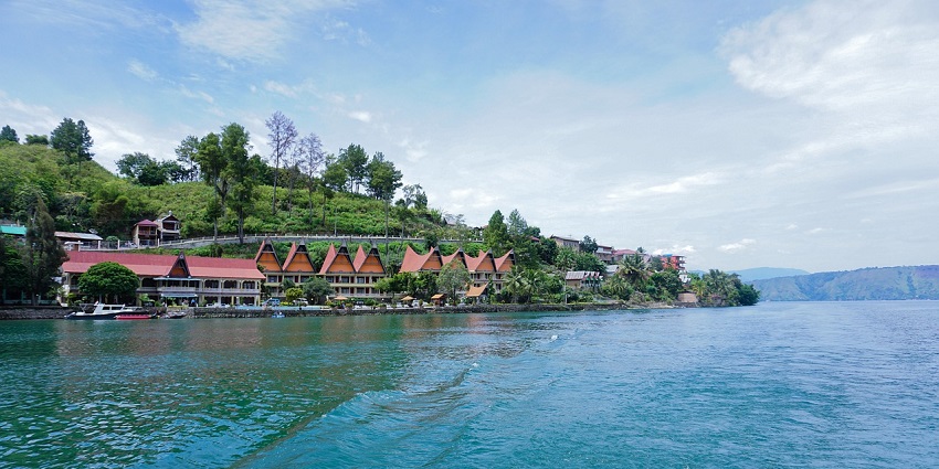 Peaceful lake view with tall pine trees and hills, amongst the top places to visit in Indonesia in December.