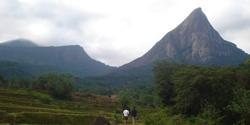 Lakgala rock with a tall rock peak, dense clouds, and lush greenery, in Sri Lanka
