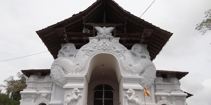 The entrance of Lankatilaka Temple is surrounded by lush foliage and stonework