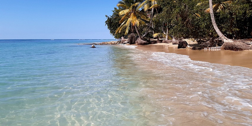 Serene tropical beach with calm blue water, distant green hills, one of the famous places to visit in Dominican Republic