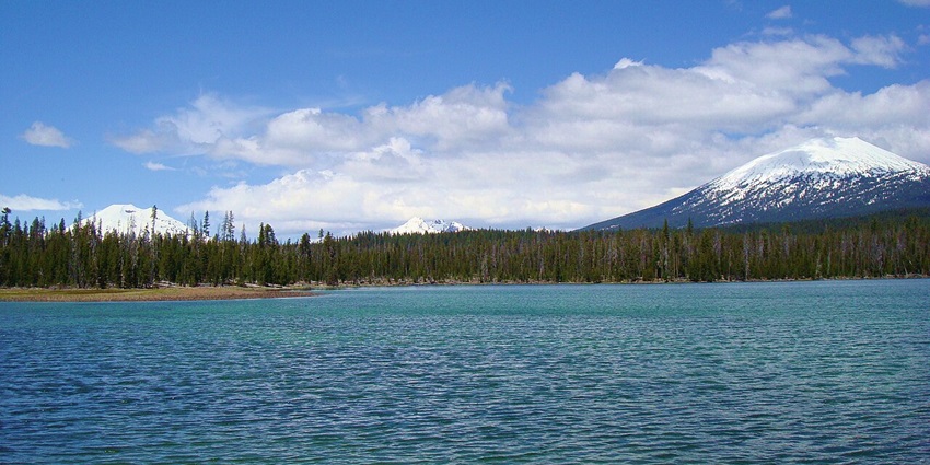 Lava lake with a large clear blue water body, distant tall green trees and snowy mountains