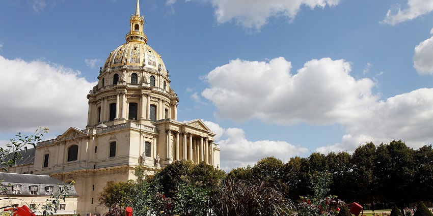 The golden dome of Les Invalides in Paris, with formal gardens and cloudy blue sky behind.