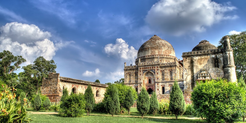 Sunlight filtering through trees in Lodhi Garden with ancient tombs in the background.