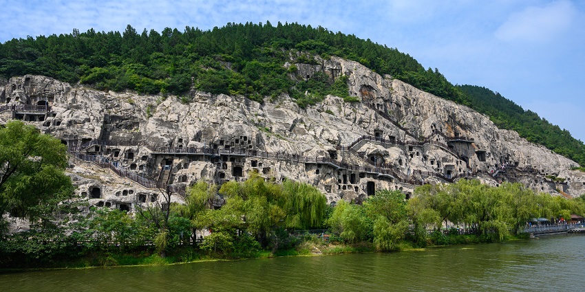 Longmen Grottoes with multiple cave entrances, a platform for walking and multiple green trees
