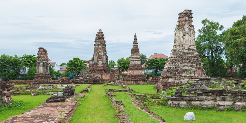 Ancient brick temple ruins with worn walls and windows surrounded by grass and trees, one of the historical places in Thailand.