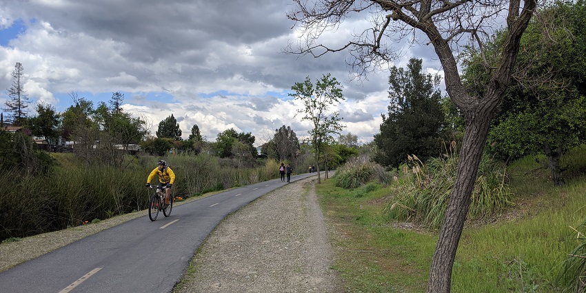 Los Gatos Creek trail with a man cycling on the trail and people walking at a distance.