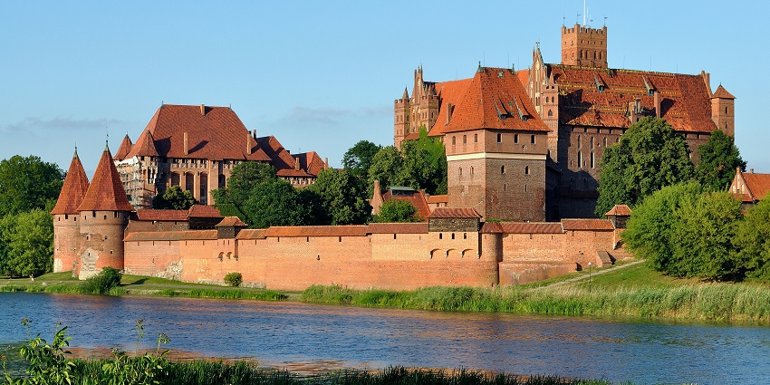 Malbork castle with traditional Polish architecture, a small water body and green trees