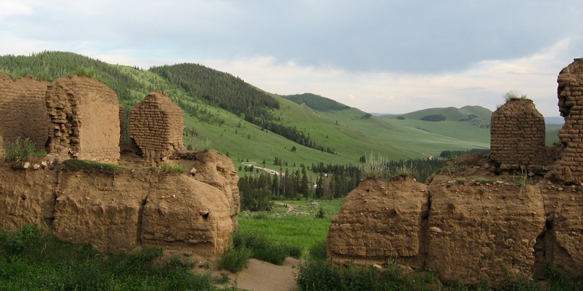 Manzushir monastery ruins with old ruined structures and green mountains in the back