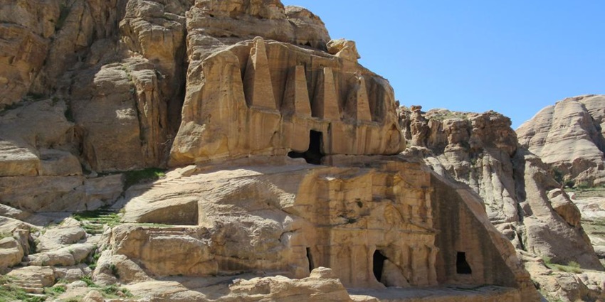 Tomb in Jordan with rocky cliffs, mountains, small entrances and partial green grasses