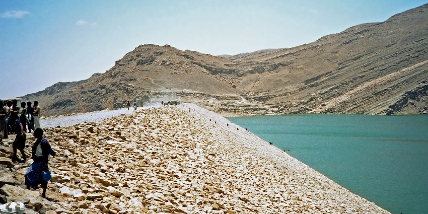 A large stone dam structure with arid hills and sparse vegetation, one of the historical places in Yemen.