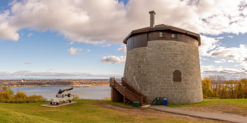 Explore the historic Martello Tower standing strong on the grassy land under a partly cloudy sky.
