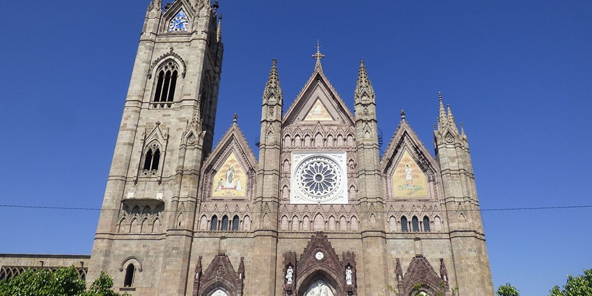 Gothic-style church with tall clock tower, rose window, and ornate stone carvings.