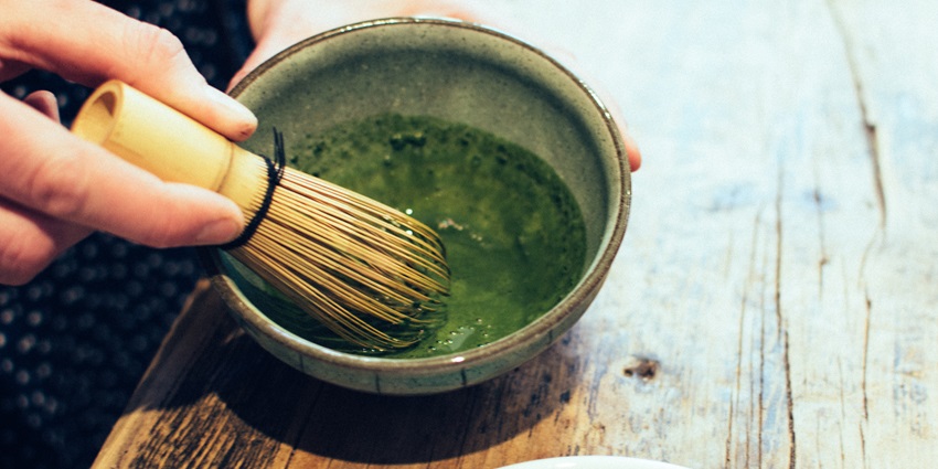 Matcha powder in a bowl with a bamboo whisk beside a traditional ceramic teacup—tasty things to buy in Tokyo.